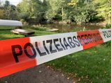 Ein Polizeiabsperrband im Vordergrund, ein Shotterweg mit Gras am Rand, im Hintergrund ein umgedrehtes Ruderboot 